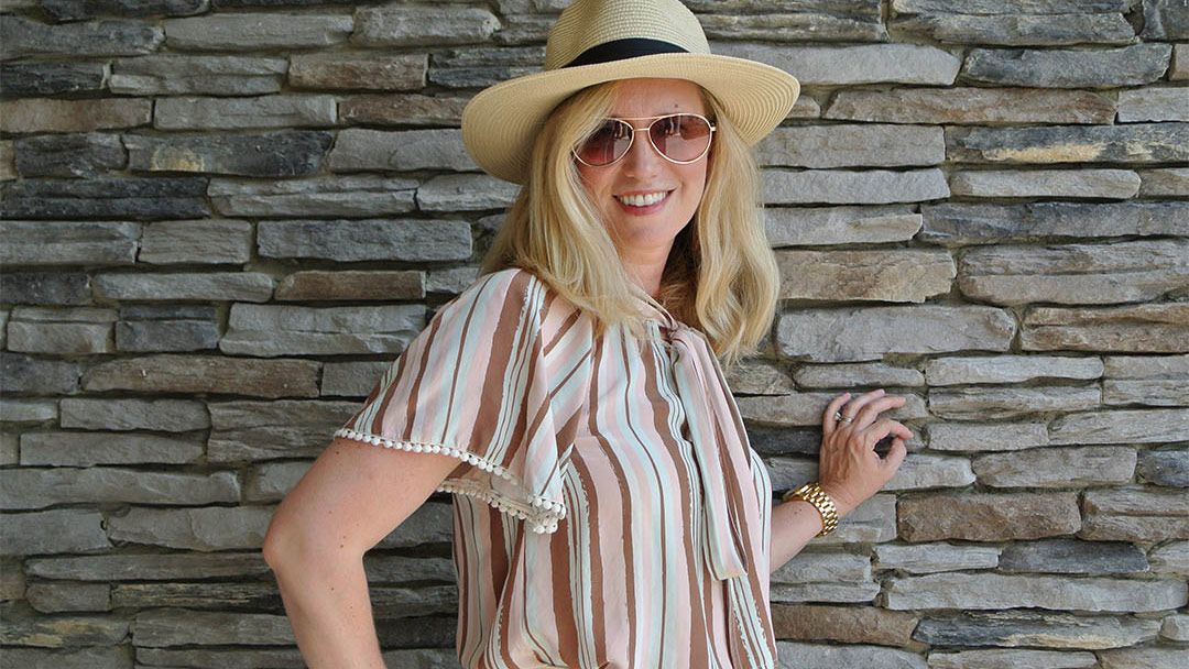 Laura wearing a vertically striped Raoul Blouse and a hat and sunglasses