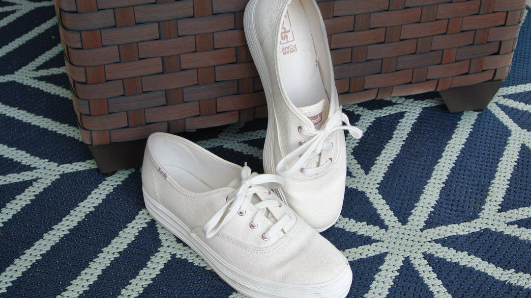 white platform Keds displayed on a blue rug and one shoe leaning against a brown woven basket