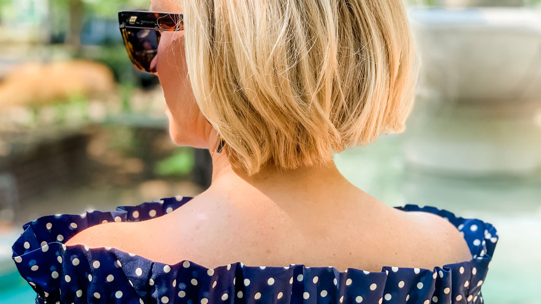 Navy and white polka dot shirt back view off the shoulder with sunglasses in tortoiseshell