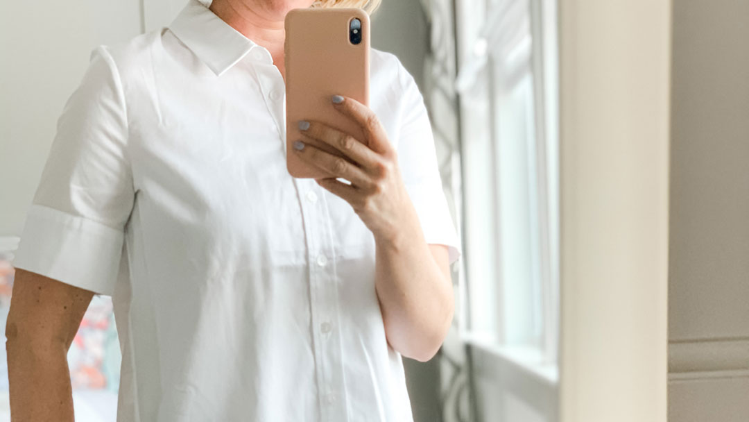 White short sleeved button down shirt on woman holding phone for mirror selfie